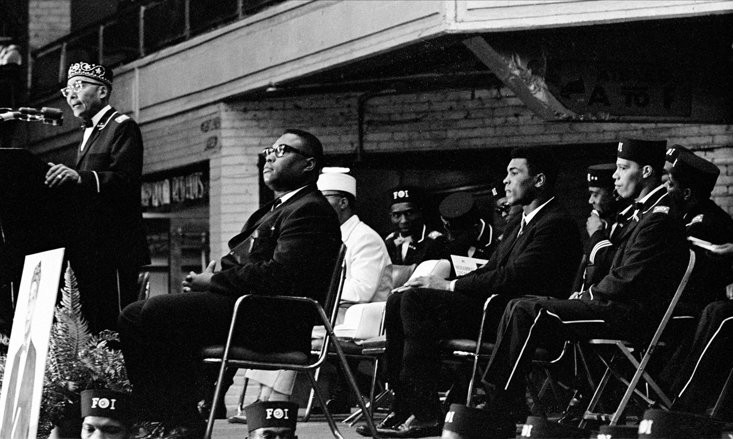 ALI WATCHES ON AS ELIJAH MUHAMMAD SPEAKS AT SAVIOUR'S DAY IN 1966